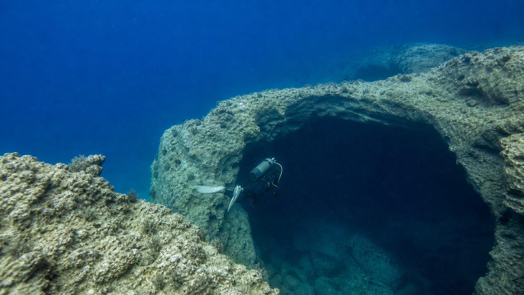 Diver swimming through the limestone arch of an illustrative Blue Hole scene